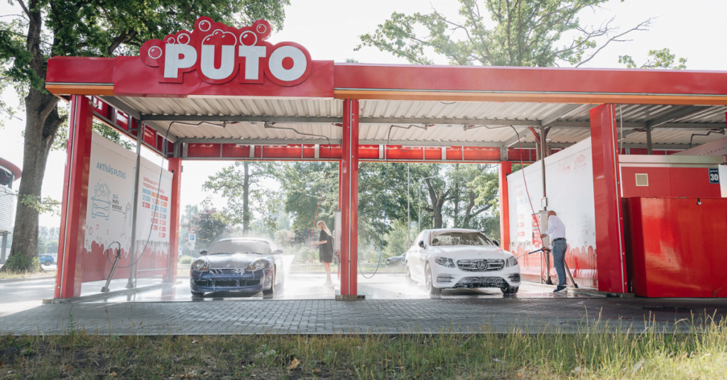 PUTO car wash - two cars are pressure washed inside red carwash bays in summer.